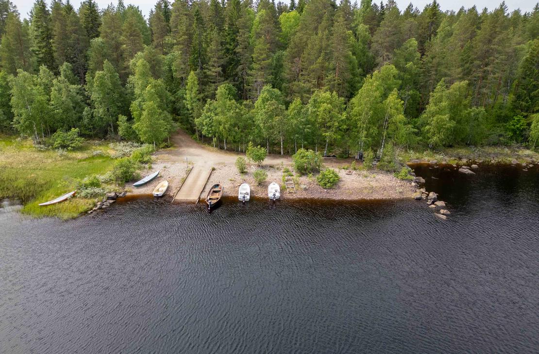 Ilmakuva järven rannassa sijaitsevasta venevalkamasta ja betoniluiskasta. Rannassa on useita veneitä ja sitä ympäröi tiheä vihreä metsä.