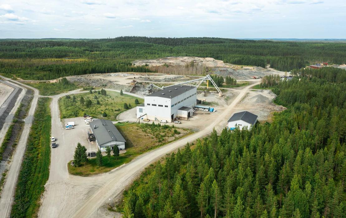Ilmakuva Pampalon kaivokselta, joka esittää teollisuusalueen sijaintia tiheän metsän ympäröimänä. Keskellä on suuri, valkoinen jalostus- tai hallirakennus ja sen ympärillä piha-alueita sekä hiekkaisia teitä. Oikealla taustalla näkyy suuri, avoin louhosalue. Koko aluetta ympäröi tiheä, tummanvihreä havumetsä.