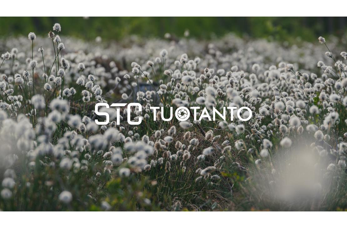 Lähikuva nevasta tai niitystä, joka on täynnä valkoisia, pörröisiä tupasvillan tai suopursun kukintoja. Kukat peittävät koko kuvan alan. Kuvan päällä lukee valkoisella, läpikuultavalla tekstillä "STC TUOTANTO", ja T-kirjainten välissä on pieni pyöreä logo.