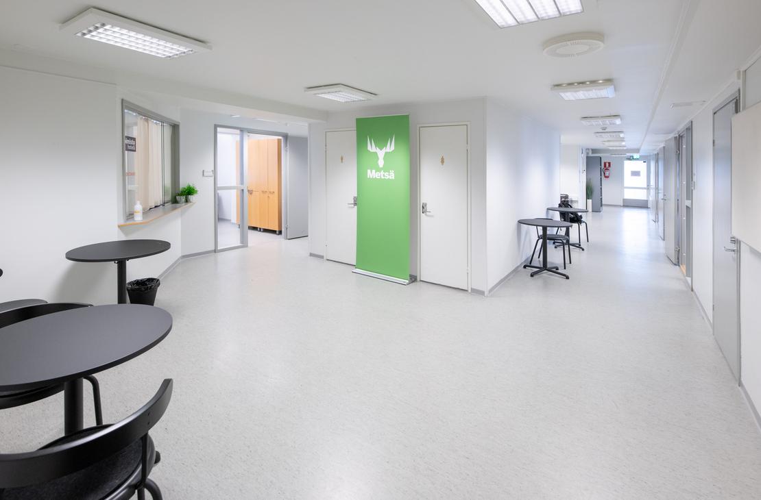 uva esitt&auml;&auml; Liikekulman Toimistohotellin modernia ja valoisaa k&auml;yt&auml;v&auml;&auml; tai aulatilaa. K&auml;yt&auml;v&auml;ss&auml; on vaalea lattia ja valkoiset sein&auml;t. Vasemmalla etualalla on py&ouml;reit&auml;, mustia p&ouml;yti&auml; tuoleineen. Keskell&auml; n&auml;kyy kirkkaan limevihre&auml; ovi, jossa on logo (mahdollisesti yrityksen tunnus), ja taaempana oranssin ja keltaisen s&auml;vyisi&auml; oviaukkoja. Oikealla on pitk&auml;, valkoinen k&auml;yt&auml;v&auml;, jossa on ty&ouml;p&ouml;yti&auml;.