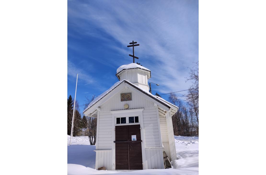 Pieni valkoinen puurakennus, mahdollisesti tsasouna, jonka katolla on ortodoksinen risti. Rakennus sijaitsee lumisessa ympäristössä kirkkaan sinisen taivaan alla.