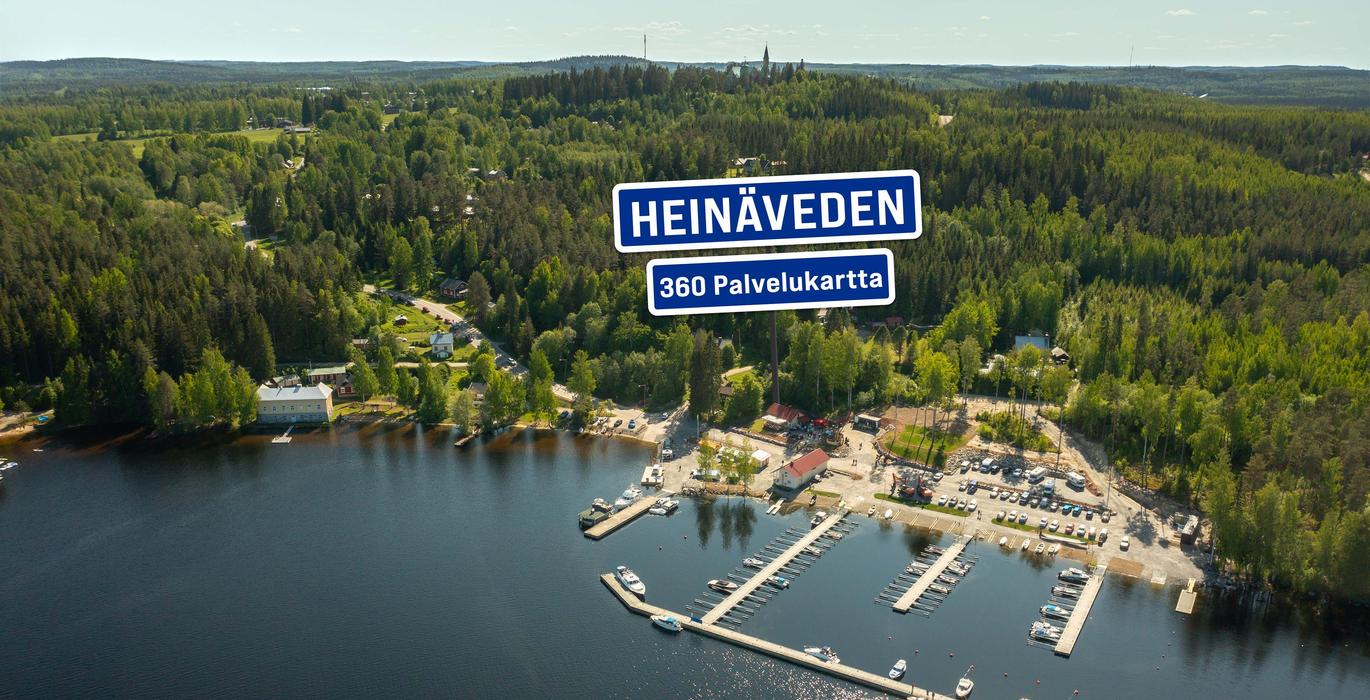 Ilmakuva Heinäveden satamasta, jossa on venelaitureita ja pysäköintialue järven rannalla. Taustalla näkyy laaja, metsäinen vaaramaisema. Kuvan päällä on sininen kyltti "HEINÄVEDEN 360 Palvelukartta".