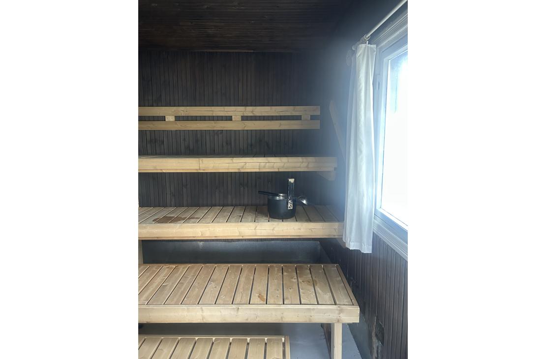 Saunan sisätila, jossa vaaleat puuseinät, lauteet ja pieni ikkuna, josta siivilöityy valoa sisään.