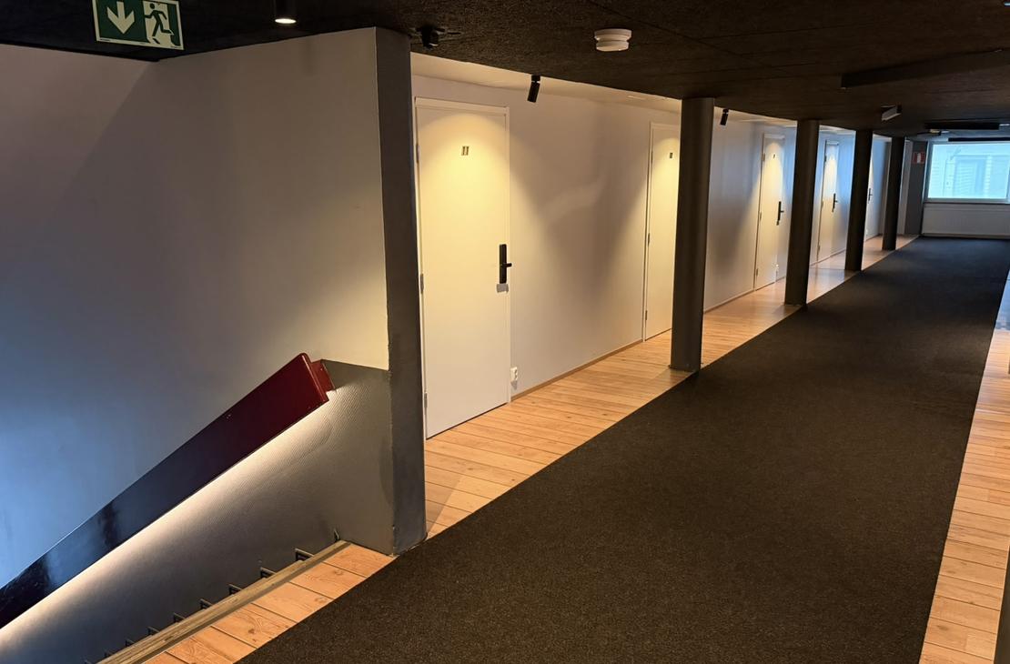 Majoitustilojen käytävä ja alas johtava valaistu porraskäytävä hätäpoistumisvaloineen. Vasemmalla näkyy huoneen numero 11 ovi.