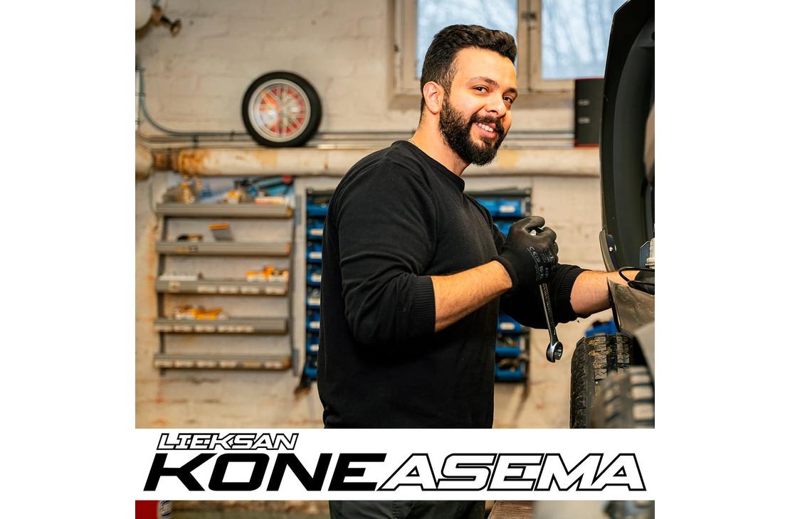 Parrakas mekaanikko hymyilee kameralle kiintoavain kädessään korjaamolla ajoneuvon äärellä. Kuvan alalaidassa on Lieksan Koneasema -tekstilogo.