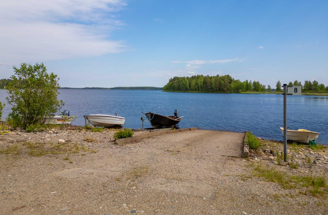 Näkymä sorapäällysteiseltä veneenlaskupaikalta järvelle. Rannassa on betonisluiska, muutamia pienveneitä sekä opastepylväs, jossa on numero 8.