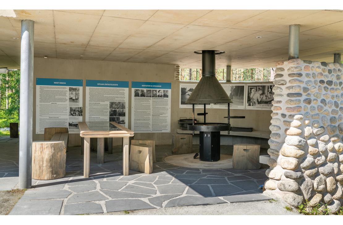 Sis&auml;kuva &Ouml;ykk&ouml;senvaaran taistelualueen taukopaikasta/museorakennuksesta. Kuvassa n&auml;kyy moderni, kivetty lattia, jolla on grillauspaikka tai takka suuren mustan liesituulettimen alla. Sein&auml;ll&auml; on kolme infotaulua teksteineen ja mustavalkokuvineen. Edess&auml; on yksinkertainen puinen p&ouml;yt&auml; ja istuimina toimivia puunrunkoja. Oikealla n&auml;kyy luonnonkivill&auml; verhoiltu pilarin osa. Tila on valoisa ja katettu.