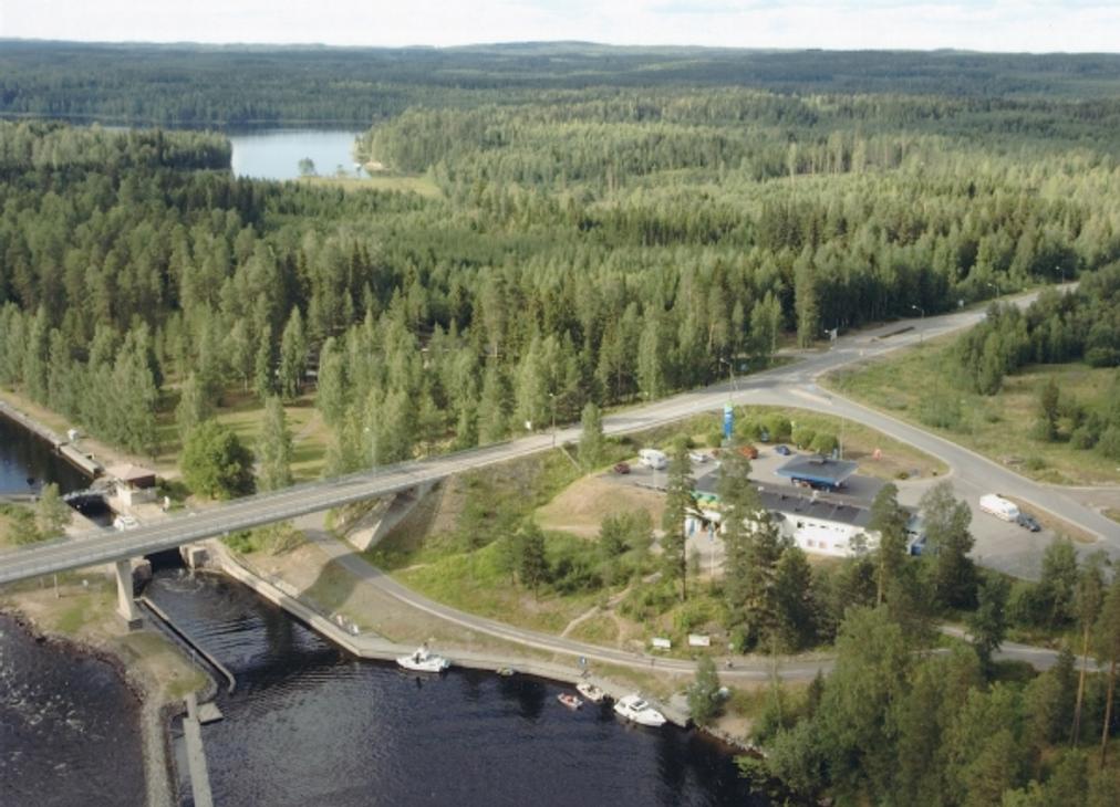 Ilmakuva Karvion kanavalta, jossa valtatie 23 ylitt&auml;&auml; kanavan siltaa pitkin. Kuvassa n&auml;kyy etualalla kanavan sulkuportteja ja laitureihin kiinnitettyj&auml; veneit&auml;. Tien vieress&auml; sijaitsee Neste Karvionkanava -huoltoasema rakennuksineen ja parkkialueineen. Taustalla avautuu laaja ja vehre&auml; mets&auml;maisema sek&auml; kaukana siint&auml;v&auml; vesist&ouml;.