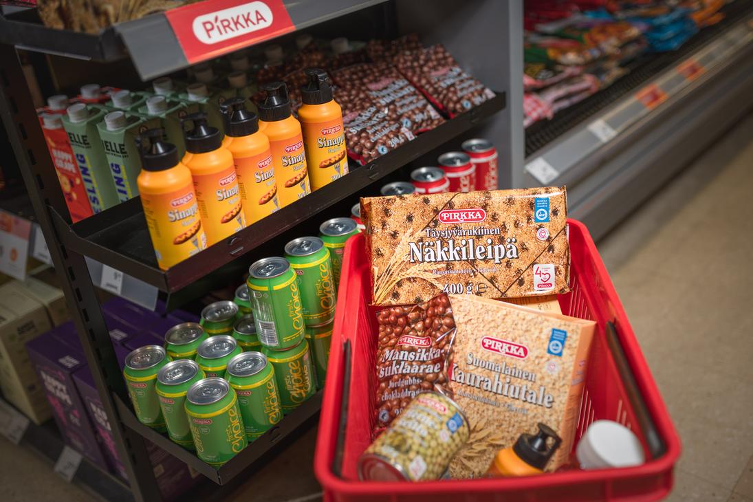 Punainen ostoskori t&auml;ynn&auml; Pirkka-merkkisi&auml; elintarvikkeita K-Market Ilomantsissa. Korissa on muun muassa Pirkka T&auml;ysjyv&auml;rukiinen N&auml;kkileip&auml;, Suomalainen Kaurahiutale ja Mansikkasuklaarae-pussi. Korin vieress&auml; on myym&auml;l&auml;n hylly, jossa on esill&auml; Pirkka-sinappeja ja vihreit&auml; juomat&ouml;lkkej&auml; punaisen Pirkka-kyltin alla.