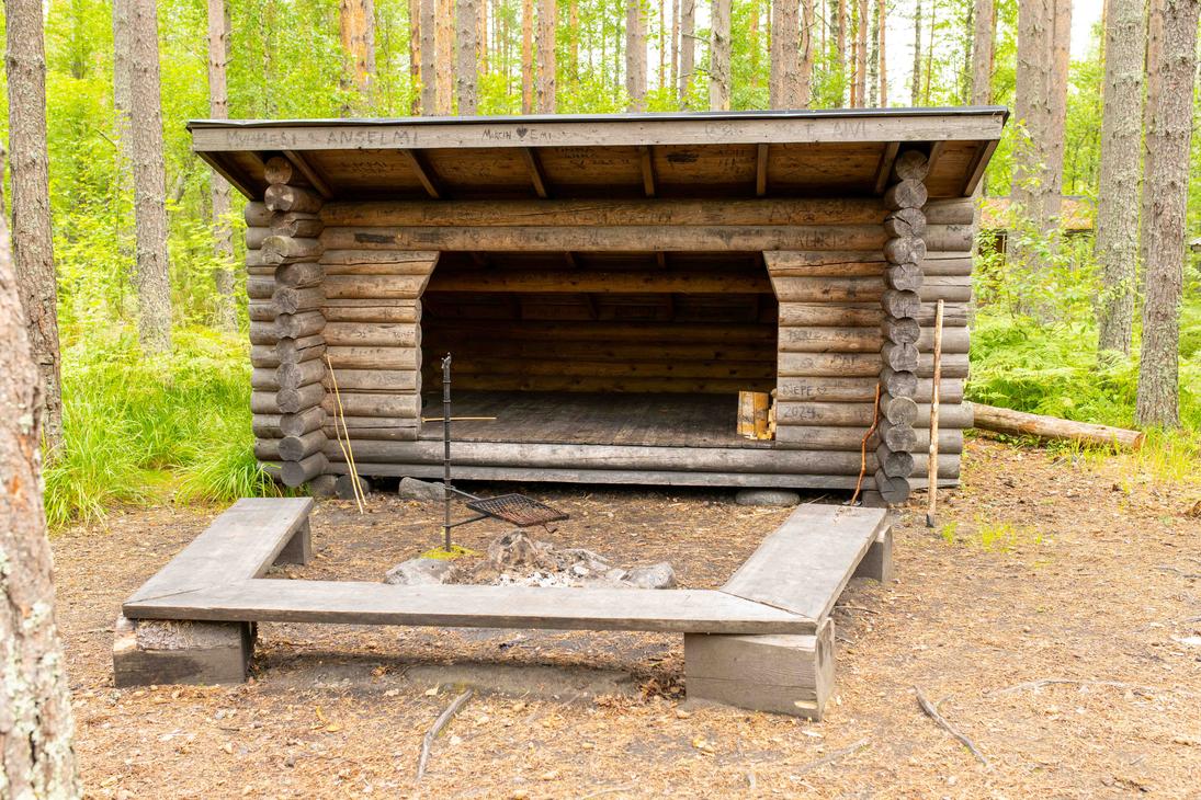 Kookas hirsirakenteinen laavu, jonka edustalla on kivestä tehty nuotiopaikka, grilliritilä ja puupenkit. Laavun hirsipintoihin on kaiverrettu nimikirjoituksia.
