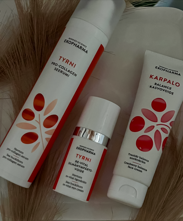 Kuvassa on Tyrni-sarjan Pro-Collagen -seerumi ja elvyttävä kasvovoide sekä Karpalo-sarjan Balance-kasvovoide. Tuotepakkaukset ovat valkoisia, ja niissä on oransseja ja punaisia graafisia marjakuvioita. Taustalla näkyy koristeellisia kuivattuja heiniä.