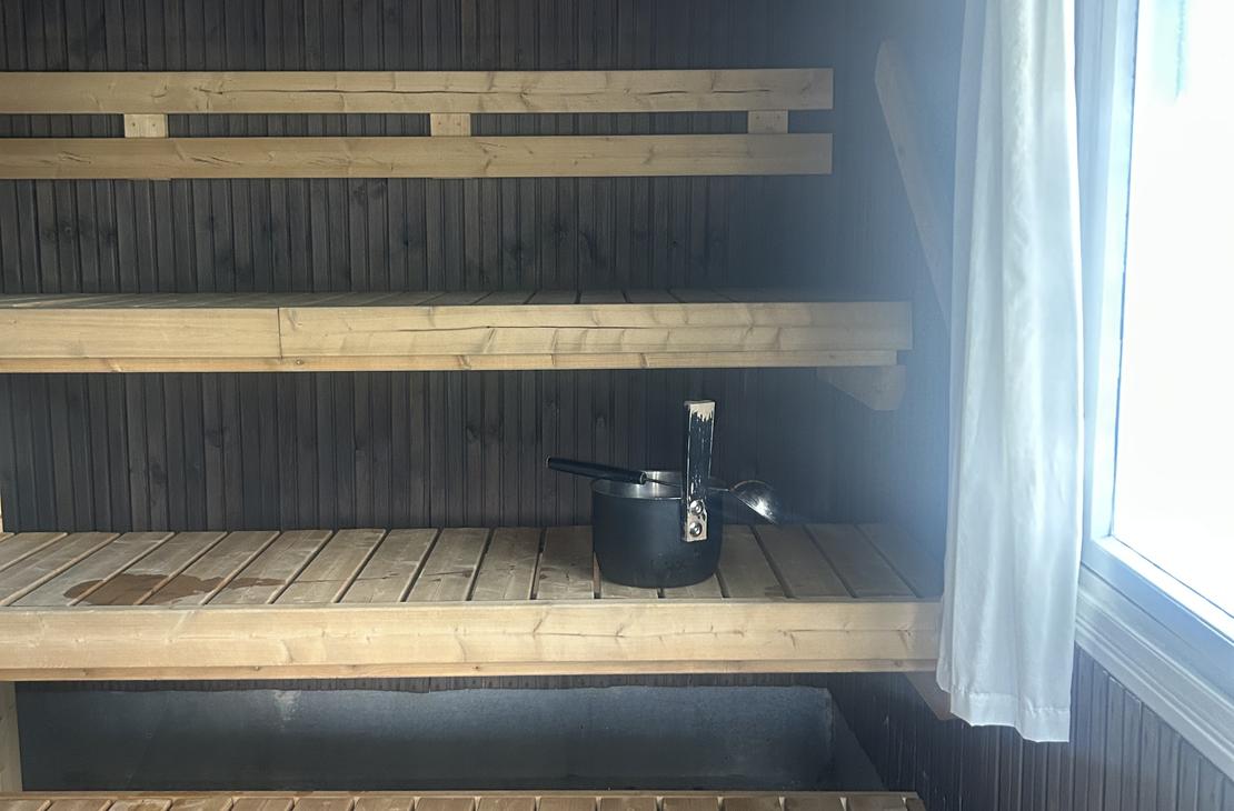 Saunan sisätila, jossa vaaleat puuseinät, lauteet ja pieni ikkuna, josta siivilöityy valoa sisään.