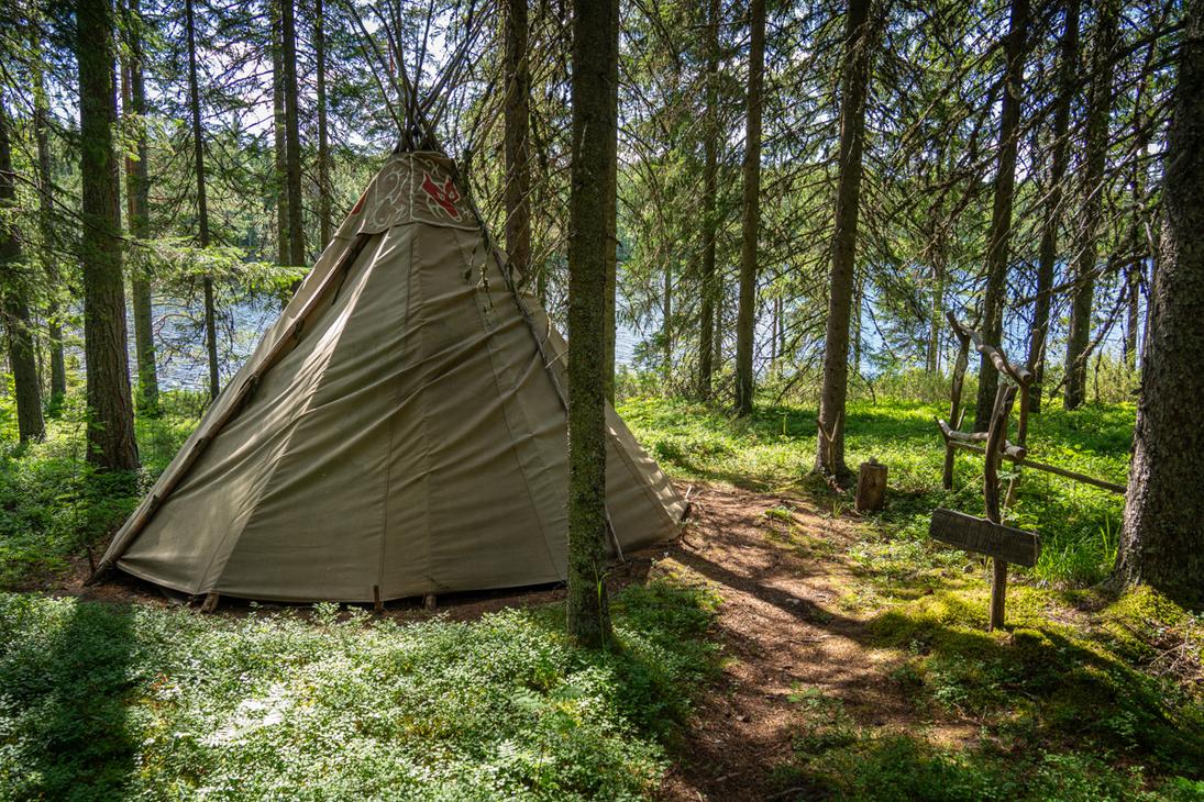 Kangaspäällysteinen kota pystytettynä tiheään havumetsään. Kodan yläosassa on punainen eläinkuvio, ja sen vieressä kulkee polku varvikon halki.