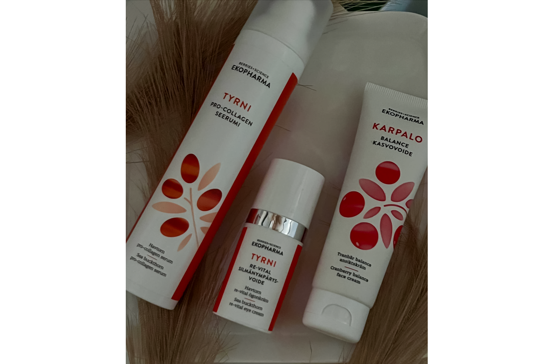 Kuvassa on Tyrni-sarjan Pro-Collagen -seerumi ja elvyttävä kasvovoide sekä Karpalo-sarjan Balance-kasvovoide. Tuotepakkaukset ovat valkoisia, ja niissä on oransseja ja punaisia graafisia marjakuvioita. Taustalla näkyy koristeellisia kuivattuja heiniä.
