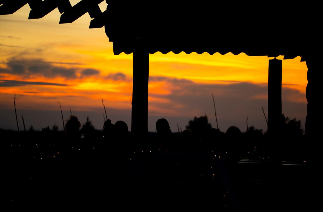 Ravintola Parppeinpirtti, Ihmisten ja rakennuksen katon siluetteja voimakkaan oranssinkeltaista auringonlaskun taivasta vasten.