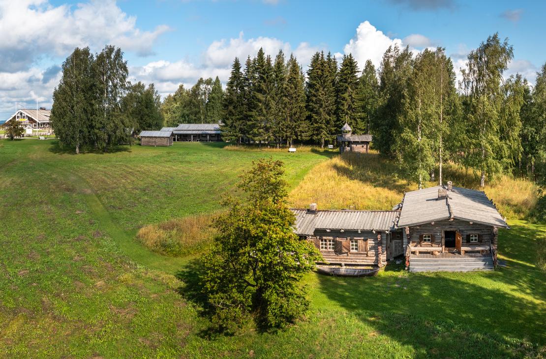  Laaja panoraamakuva, joka esitt&auml;&auml; Rajakenraalin majaa, perinteist&auml; hirsim&ouml;kki&auml; tai -rakennusta, joka sijaitsee avoimessa, kumpuilevassa maastossa. Rakennus on keskell&auml; oikealla ja sen edess&auml; on vihre&auml; nurmikentt&auml;. Alueella on runsaasti puita, erityisesti koivuja ja havupuita, ja taustalla avautuu maisema, jossa on lis&auml;&auml; rakennuksia ja peltoa. Taivas on sininen ja pilvinen.