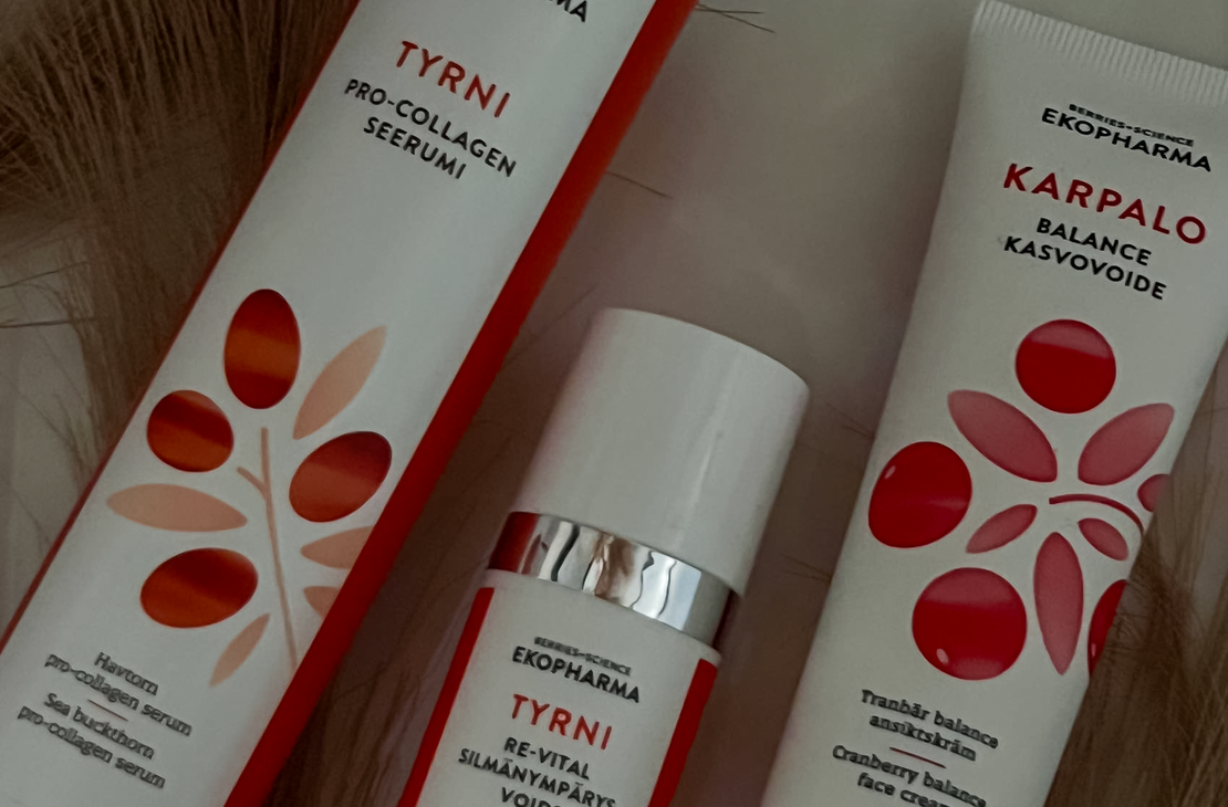 Kuvassa on Tyrni-sarjan Pro-Collagen -seerumi ja elvyttävä kasvovoide sekä Karpalo-sarjan Balance-kasvovoide. Tuotepakkaukset ovat valkoisia, ja niissä on oransseja ja punaisia graafisia marjakuvioita. Taustalla näkyy koristeellisia kuivattuja heiniä.