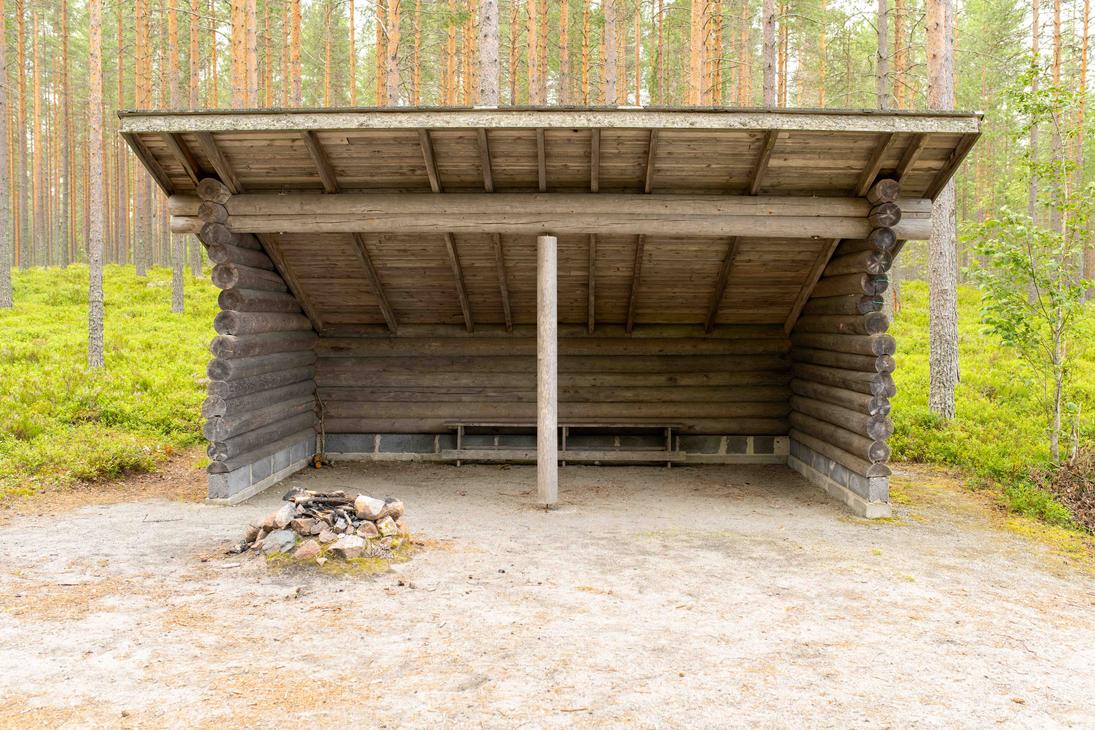 Suuri hirsirakenteinen laavu m&auml;ntymets&auml;n siimeksess&auml;. Laavun edustalla hiekalla on kivist&auml; koottu nuotiopaikka ja sis&auml;ll&auml; pystytuki sek&auml; puupenkki.