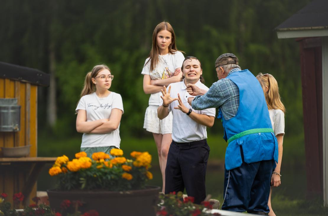 M&ouml;hk&ouml;n kes&auml;teatterin Peitetarina-n&auml;ytelm&auml;n kohtaus, jossa siniseen liiviin pukeutunut vanhempi mies elehtii l&auml;hell&auml; valkoiseen poolopaitaan pukeutunutta nuorta miest&auml;, joka tekee torjuvan k&auml;sieleen kasvot h&auml;t&auml;&auml;ntyneen&auml;. Taustalla kolme nuorta naista seuraa tilannetta vakavina, ja etualalla ruukussa kukkii oransseja samettikukkia.