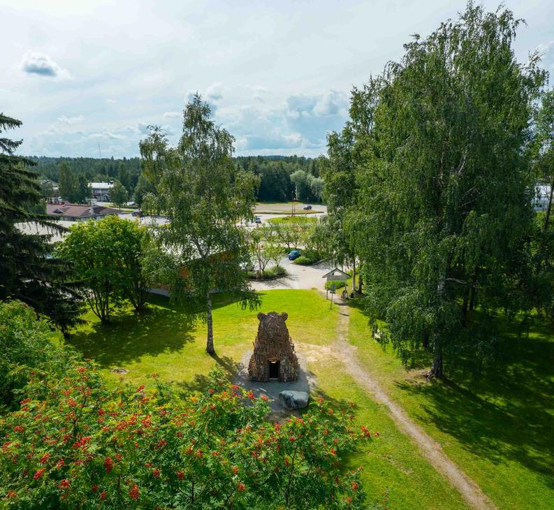 Ilmakuva suuresta, puusta tehdystä karhupatsaasta, ILOKARHU -nimisestä veistoksesta Ilomantsista. Karhu on koottu useista pienemmistä puupaloista ja laudoista. Kuvassa näkyy selvästi karhun karkea pintakerros. Taustalla on Ilomantsin tori.
