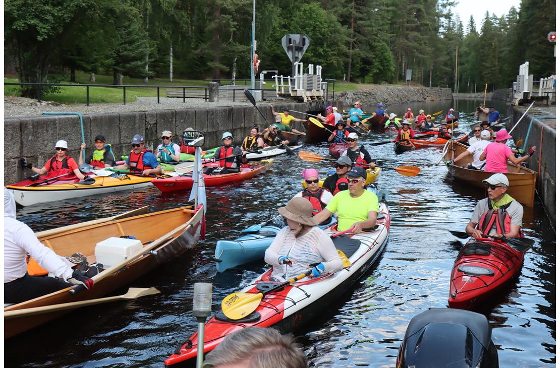 Kanava-allas täynnä värikkäitä kajakkeja, kanootteja ja soutuveneitä odottamassa sulutusta. Retkeilijöillä on yllään kelluntaliivit.