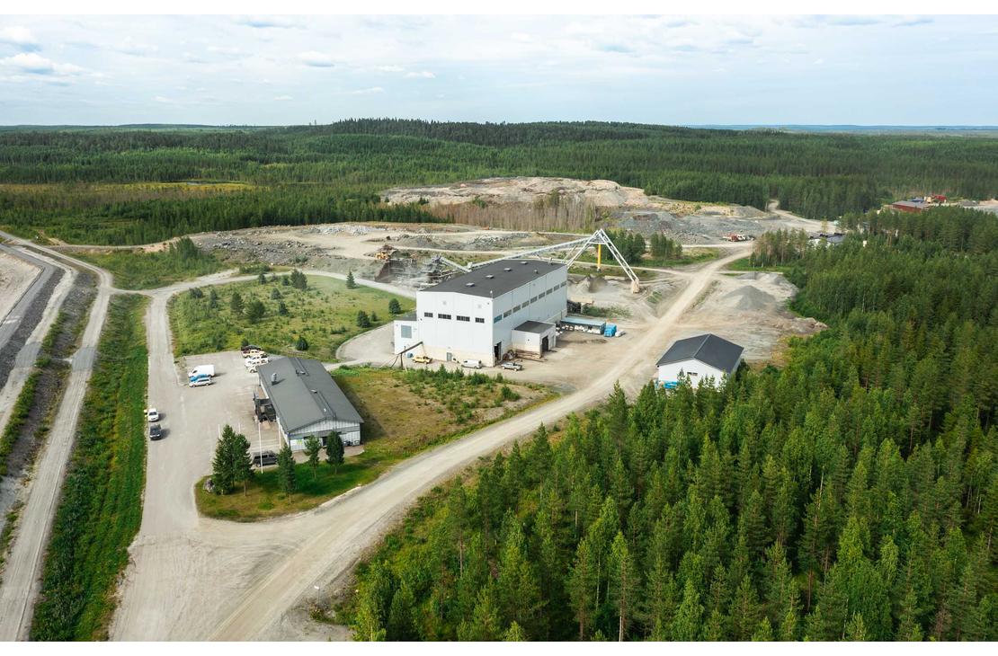 Ilmakuva Pampalon kaivokselta, joka esittää teollisuusalueen sijaintia tiheän metsän ympäröimänä. Keskellä on suuri, valkoinen jalostus- tai hallirakennus ja sen ympärillä piha-alueita sekä hiekkaisia teitä. Oikealla taustalla näkyy suuri, avoin louhosalue. Koko aluetta ympäröi tiheä, tummanvihreä havumetsä.