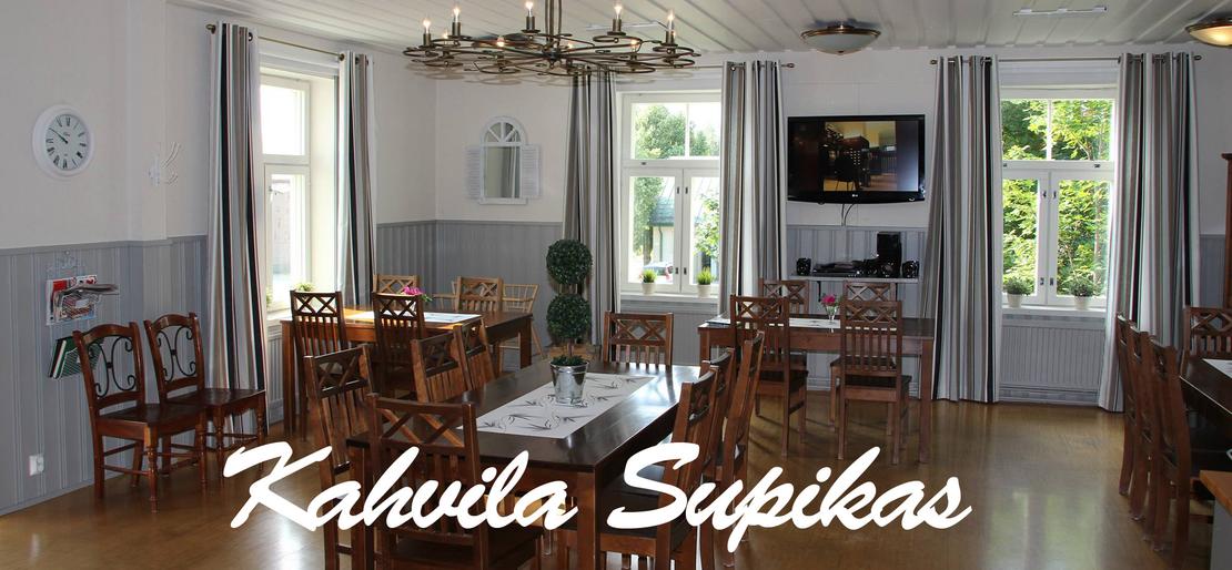 Kuva esittää Kahvila Supikkaan sisätiloja. Tila on valoisa ja siinä on useita suuria ikkunoita harmailla verhoilla. Seinät ovat kaksiväriset: alaosa on harmaa ja yläosa valkoinen. Huoneessa on useita puisia pöytiä ja tuoleja, ja pöydillä on valkoiset liinat. Oikealla on seinällä taulutelevisio. Kuvan alaosassa on suuri, valkoisella, kursivoidulla fontilla teksti "Kahvila Supikas".