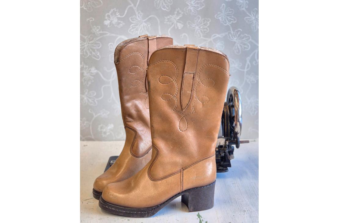 Pari klassisia, vaaleanruskeita nahkasaappaita, joissa on koristeellisia tikkauksia varressa ja maltillinen koro.