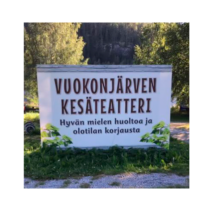 Kuva esittää Vuokonjärven Kesäteatterin opaskylttiä ulkona luonnon helmassa. Kyltti on suorakulmainen ja valkoinen. Siinä lukee tummanruskealla, isolla fontilla kaksi riviä: "VUOKONJÄRVEN" ja "KESÄTEATTERI". Sen alapuolella on pienemmällä, mustalla tekstillä tunnuslause "Hyvän mielen huoltoa ja olotilan korjausta". Kyltti on sijoitettu nurmikolle ja soraan, ja sitä kehystää ala- ja sivuosissa vihreä lehtikuviointi. Taustalla näkyy rehevää metsää.