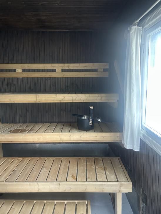 Saunan sisätila, jossa vaaleat puuseinät, lauteet ja pieni ikkuna, josta siivilöityy valoa sisään.