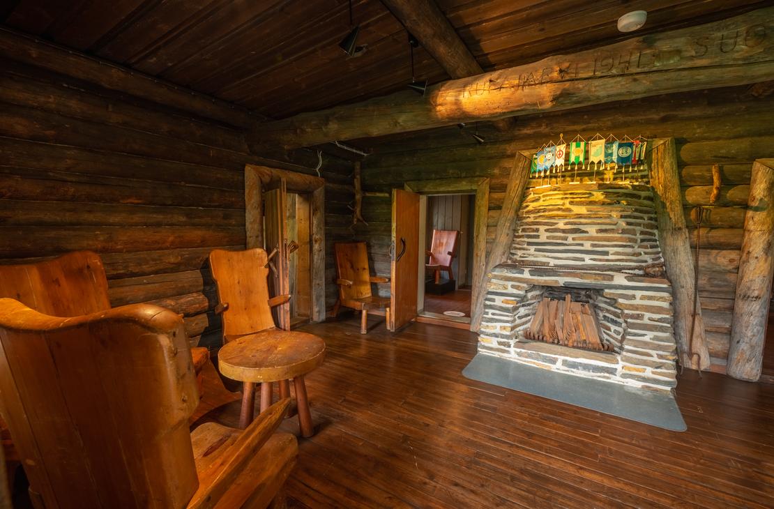 Sis&auml;kuva Rajakenraalin majan oleskelutilasta. Huone on tunnelmallinen ja siin&auml; on tummat hirsisein&auml;t sek&auml; puulattiat. Keskeisell&auml; paikalla on suuri, luonnonkivist&auml; muurattu takka. Vasemmalla n&auml;kyy kaksi nahkaverhoiltua tai puunv&auml;rist&auml; nojatuolia pienen sivup&ouml;yd&auml;n ymp&auml;rill&auml;. Takan takana on oviaukkoja, jotka johtavat muihin tiloihin. Tila on valaistu l&auml;mpim&auml;ll&auml;, pehme&auml;ll&auml; valolla.