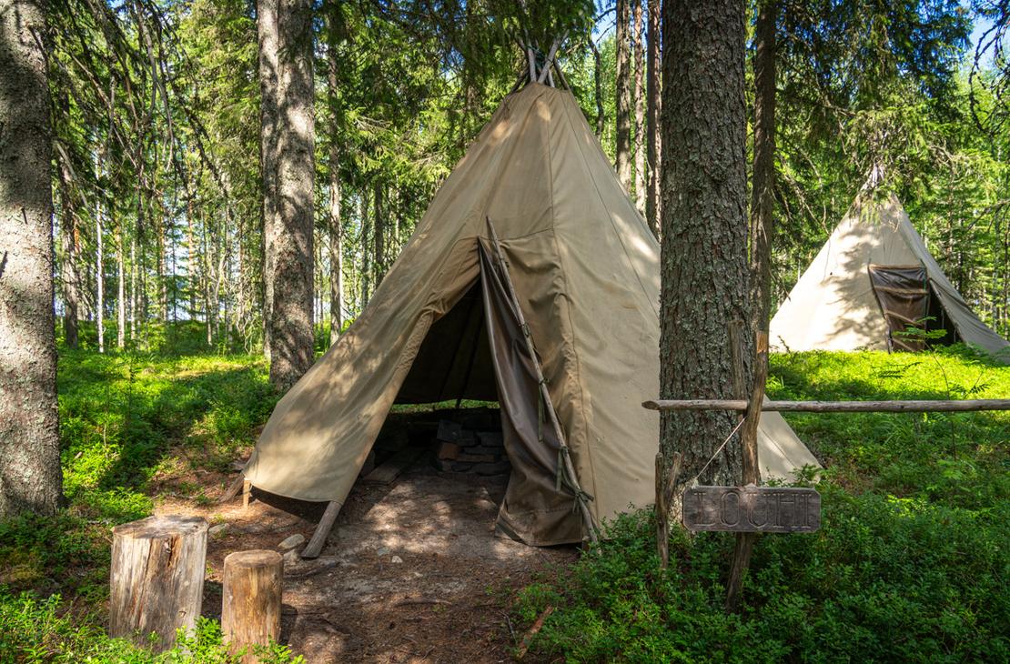 Kaksi kangaskotaa metsän siimeksessä. Etualalla olevan kodan vieressä on puinen kyltti, jossa lukee "LOUHI", ja sen edustalla on nuotiopaikka.
