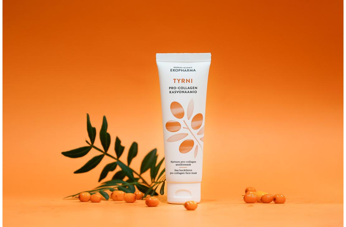 Ekopharma Tyrni Pro-Collagen -kasvonaamiotuubi oranssilla taustalla. Tuubin vieressä on vihreä tyrninoksa ja muutama tyrnimarja oranssilla alustalla.