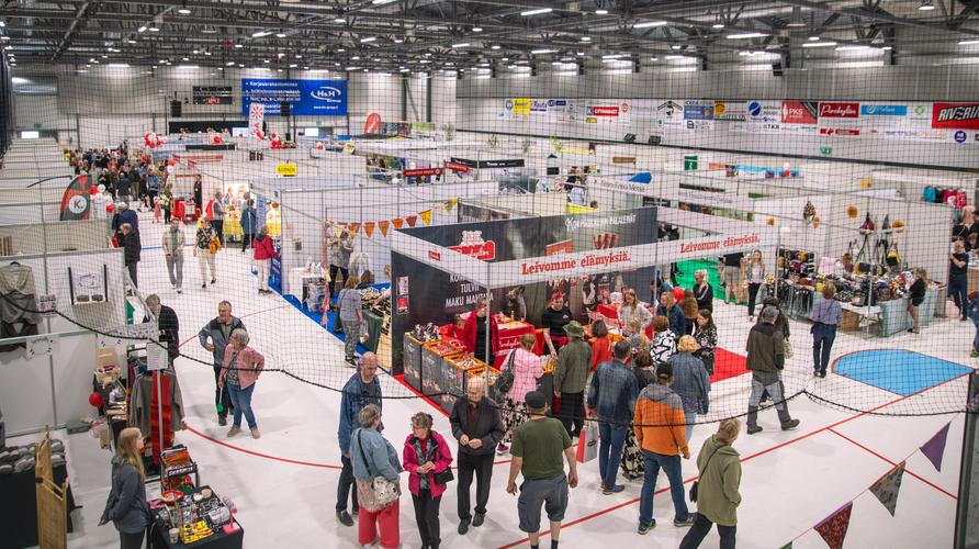 Yleiskuva suurista sisämessuista urheiluhallissa. Ihmiset kiertelevät lukuisilla messuosastoilla, joita on aseteltu kentälle.