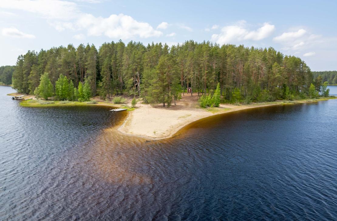 Korkealta otettu ilmakuva hiekkasärkän kärjestä ja sitä ympäröivästä järvestä. Niemenkärjessä kasvaa mäntymetsää, ja maastossa erottuu pieni punainen rakennus.