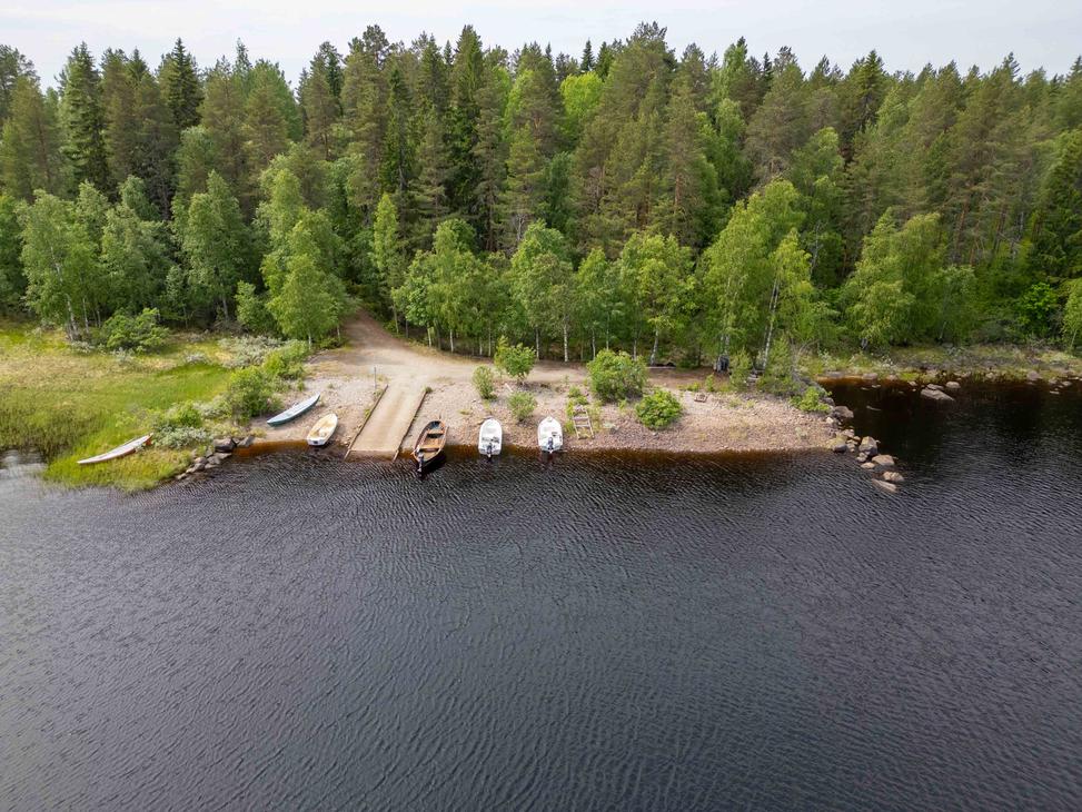 Ilmakuva järven rannassa sijaitsevasta venevalkamasta ja betoniluiskasta. Rannassa on useita veneitä ja sitä ympäröi tiheä vihreä metsä.