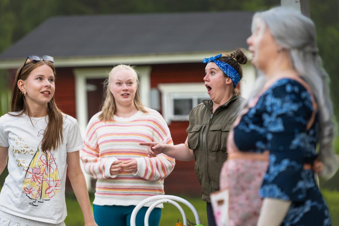 M&ouml;hk&ouml;n kes&auml;teatterin Peitetarina-n&auml;ytelm&auml;n kohtaus, jossa nelj&auml; naisn&auml;yttelij&auml;&auml; esiintyy ulkon&auml;ytt&auml;m&ouml;ll&auml; punaisen rakennuksen edustalla. Oikealla etualalla n&auml;kyy ep&auml;tarkkana sivuprofiili harmaatukkaisesta naisesta. Keskell&auml; sinip&auml;&auml;hineinen nainen osoittaa vasemmalle suu ammollaan h&auml;mm&auml;styksest&auml;, ja vasemmalla kaksi naista seuraa tilannetta ilmeikk&auml;&auml;sti.