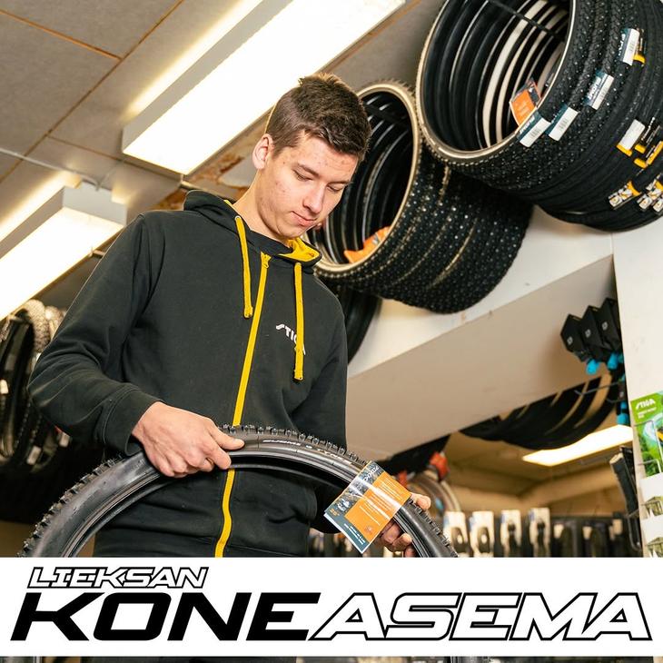 Nuori mies tutkii polkupyörän nastarengasta myymälässä rengashyllyjen edessä. Kuvan alalaidassa on Lieksan Koneasema -tekstilogo.