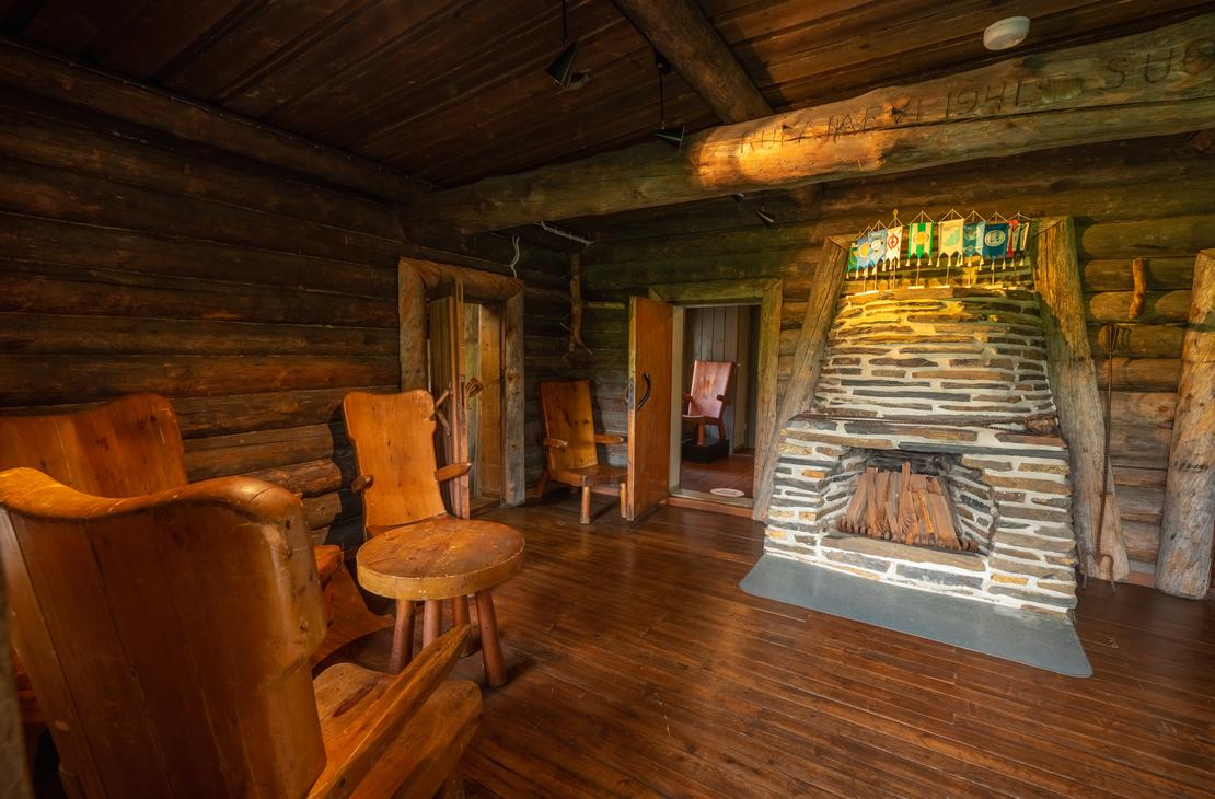 Sis&auml;kuva Rajakenraalin majan oleskelutilasta. Huone on tunnelmallinen ja siin&auml; on tummat hirsisein&auml;t sek&auml; puulattiat. Keskeisell&auml; paikalla on suuri, luonnonkivist&auml; muurattu takka. Vasemmalla n&auml;kyy kaksi nahkaverhoiltua tai puunv&auml;rist&auml; nojatuolia pienen sivup&ouml;yd&auml;n ymp&auml;rill&auml;. Takan takana on oviaukkoja, jotka johtavat muihin tiloihin. Tila on valaistu l&auml;mpim&auml;ll&auml;, pehme&auml;ll&auml; valolla.