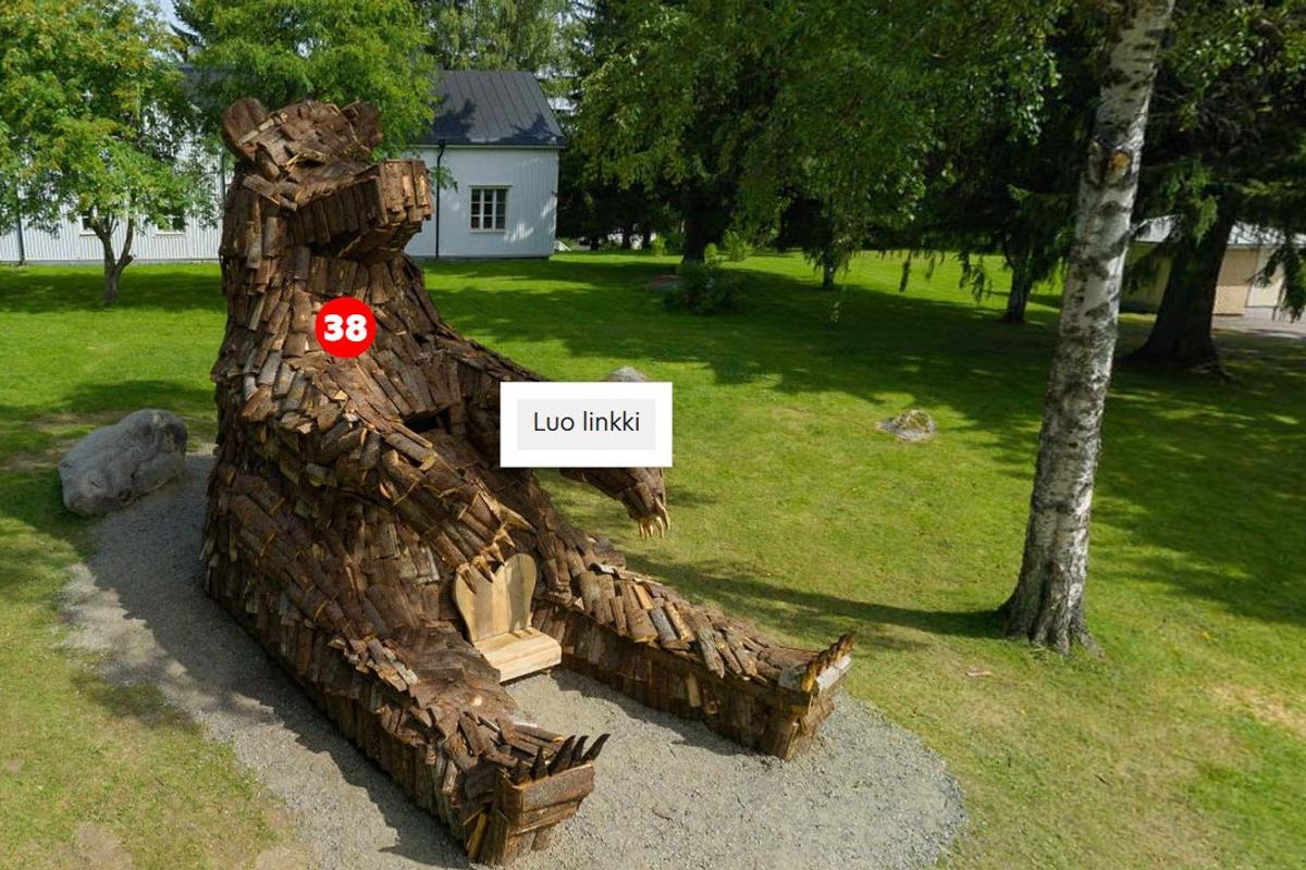 Suuri puusta tehty ILOKARUH -karhupatsas, numeroitu punaisella ympyr&auml;ll&auml; 38, istuu ja n&auml;ytt&auml;&auml; rauhalliselta kes&auml;isess&auml; nurmikkoisessa ymp&auml;rist&ouml;ss&auml;. Patasasta ymp&auml;r&ouml;iv&auml;t puut. Patsaan vieress&auml; on laatikko tekstill&auml; "Luo linkki".