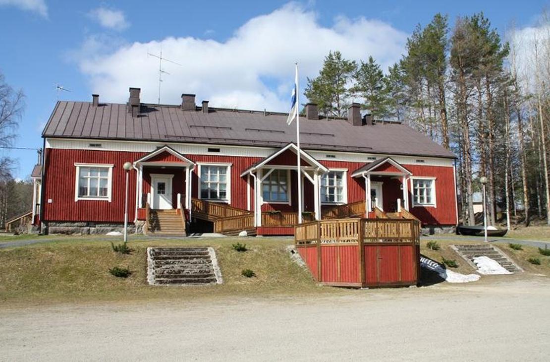 Kuva esittää matalaa, perinteistä, punamultamaalilla maalattua puutaloa, joka on todennäköisesti Mantan Majatalo. Rakennuksessa on tummanruskea katto ja useita valkoisia kuisteja, joista keskimmäisen edessä seisoo lipputanko (Suomen lippu liehuu). Kuistien edessä on puisia aitarakennelmia tai terassinreunoja. Talo on sijoitettu loivaan rinteeseen, ja sitä ympäröi niukasti kasvillisuutta sekä taustalla havupuita.