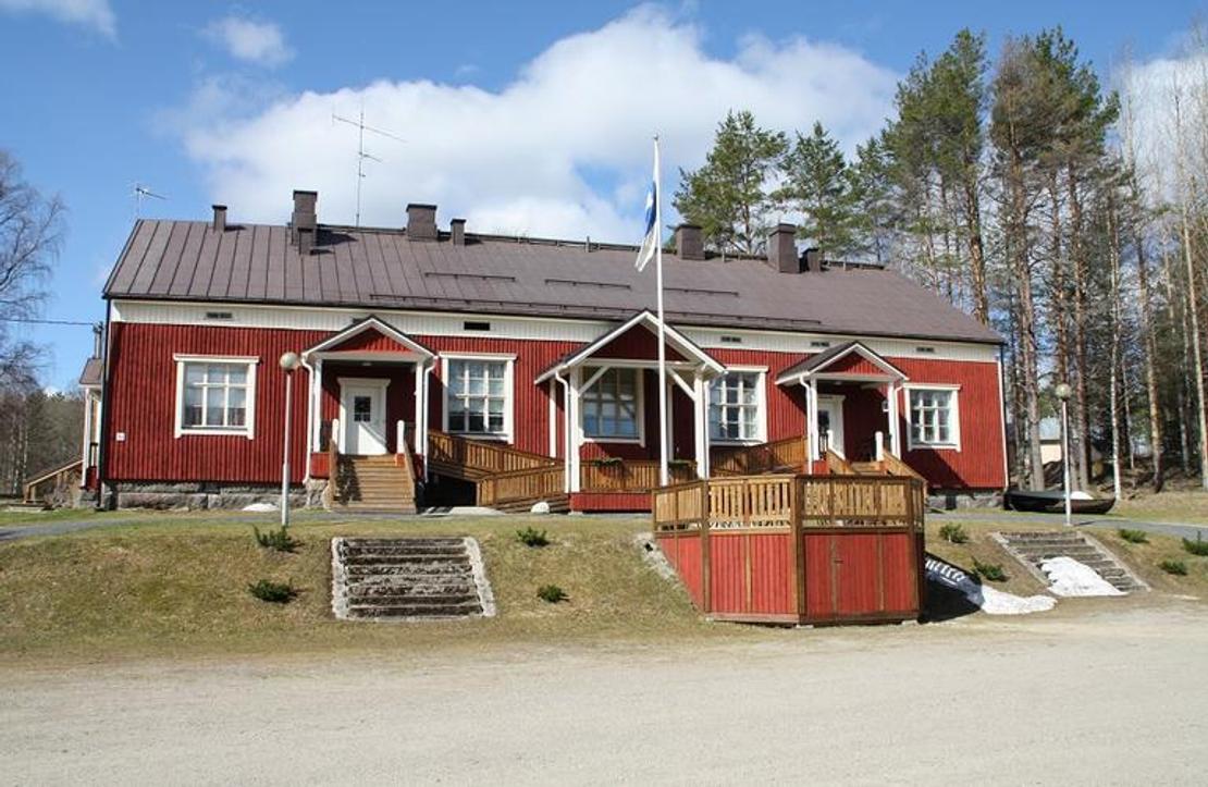 Kuva esittää matalaa, perinteistä, punamultamaalilla maalattua puutaloa, joka on todennäköisesti Mantan Majatalo. Rakennuksessa on tummanruskea katto ja useita valkoisia kuisteja, joista keskimmäisen edessä seisoo lipputanko (Suomen lippu liehuu). Kuistien edessä on puisia aitarakennelmia tai terassinreunoja. Talo on sijoitettu loivaan rinteeseen, ja sitä ympäröi niukasti kasvillisuutta sekä taustalla havupuita.