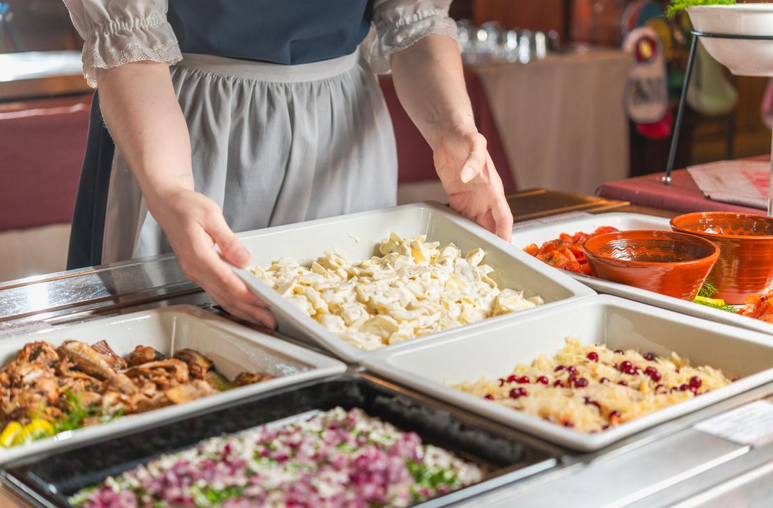 L&auml;hikuva perinneasuun pukeutuneen tarjoilijan k&auml;sist&auml;, jotka asettavat salaattivuokaa buffetp&ouml;yt&auml;&auml;n Ravintola Parppeinpirtiss&auml; Ilomantsin Parppeinvaaralla. P&ouml;yd&auml;ll&auml; on tarjoiluastioissa erilaisia kylmi&auml; ruokalajeja, kuten kalaa, pikkel&ouml;ity&auml; punasipulia ja hapankaalia puolukoilla.
