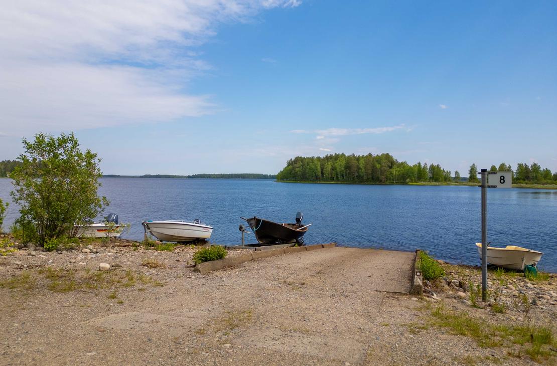 Näkymä sorapäällysteiseltä veneenlaskupaikalta järvelle. Rannassa on betonisluiska, muutamia pienveneitä sekä opastepylväs, jossa on numero 8.
