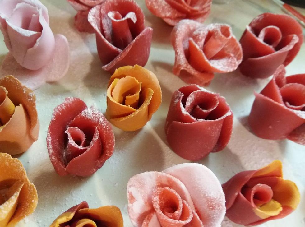 L&auml;hikuva useista sy&ouml;t&auml;vist&auml; ruusunmuotoisista koristeista tai makeisista, jotka on tehty sokerimassasta tai marsipaanista, mahdollisesti Kotipari L&auml;mmin Halaus Oy:n tuotteita. Ruusut ovat eri s&auml;vyisi&auml;, mukaan lukien vaaleanpunainen, koralli ja oranssi, ja ne on aseteltu vaalealle pinnalle.