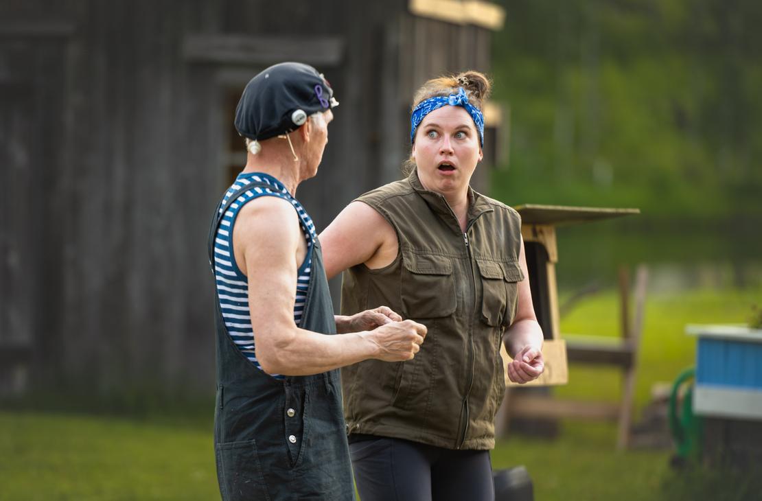 M&ouml;hk&ouml;n kes&auml;teatterin Peitetarina-n&auml;ytelm&auml;n kohtaus, jossa kaksi n&auml;yttelij&auml;&auml; esiintyy ulkon&auml;ytt&auml;m&ouml;ll&auml; vanhan puurakennuksen edustalla. Vasemmalla on raidalliseen hihattomaan paitaan, haalareihin ja mustaan p&auml;&auml;hineeseen pukeutunut mies sivuprofiilissa. Oikealla oleva nainen, jolla on sininen p&auml;&auml;huivi ja vihre&auml; liivi, katsoo miest&auml; &auml;&auml;rimm&auml;isen h&auml;mm&auml;styneen&auml; suu ammollaan.