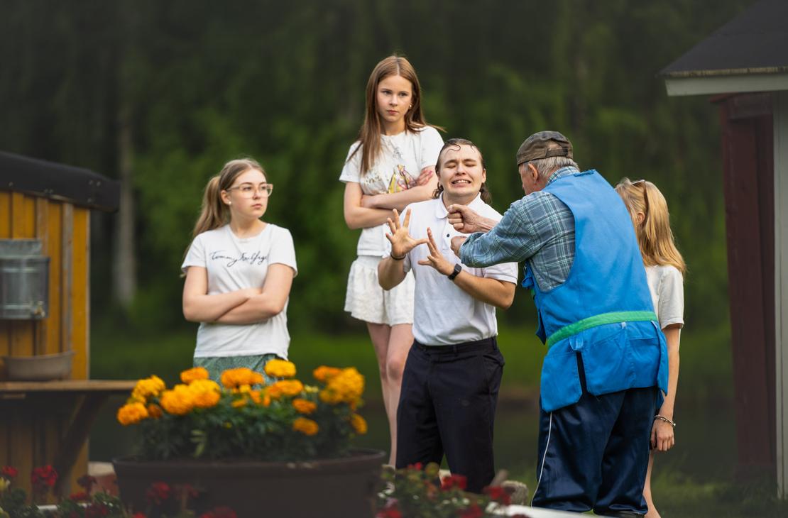 M&ouml;hk&ouml;n kes&auml;teatterin Peitetarina-n&auml;ytelm&auml;n kohtaus, jossa siniseen liiviin pukeutunut vanhempi mies elehtii l&auml;hell&auml; valkoiseen poolopaitaan pukeutunutta nuorta miest&auml;, joka tekee torjuvan k&auml;sieleen kasvot h&auml;t&auml;&auml;ntyneen&auml;. Taustalla kolme nuorta naista seuraa tilannetta vakavina, ja etualalla ruukussa kukkii oransseja samettikukkia.