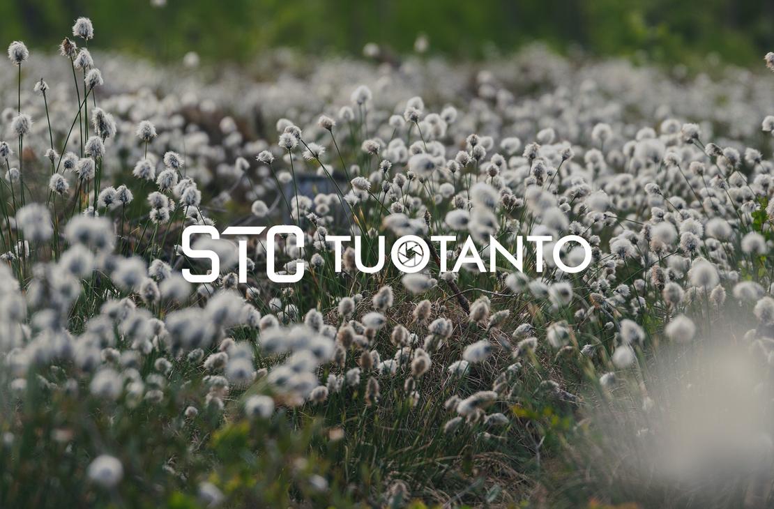 Lähikuva nevasta tai niitystä, joka on täynnä valkoisia, pörröisiä tupasvillan tai suopursun kukintoja. Kukat peittävät koko kuvan alan. Kuvan päällä lukee valkoisella, läpikuultavalla tekstillä "STC TUOTANTO", ja T-kirjainten välissä on pieni pyöreä logo.