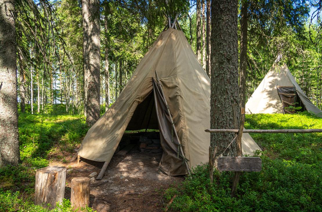 Kaksi kangaskotaa metsän siimeksessä. Etualalla olevan kodan vieressä on puinen kyltti, jossa lukee "LOUHI", ja sen edustalla on nuotiopaikka.