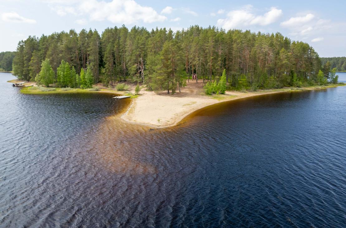 Korkealta otettu ilmakuva hiekkasärkän kärjestä ja sitä ympäröivästä järvestä. Niemenkärjessä kasvaa mäntymetsää, ja maastossa erottuu pieni punainen rakennus.